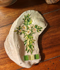 “Hand‑decorated small off‑white shell featuring a green cross accented with cheerful daisies.