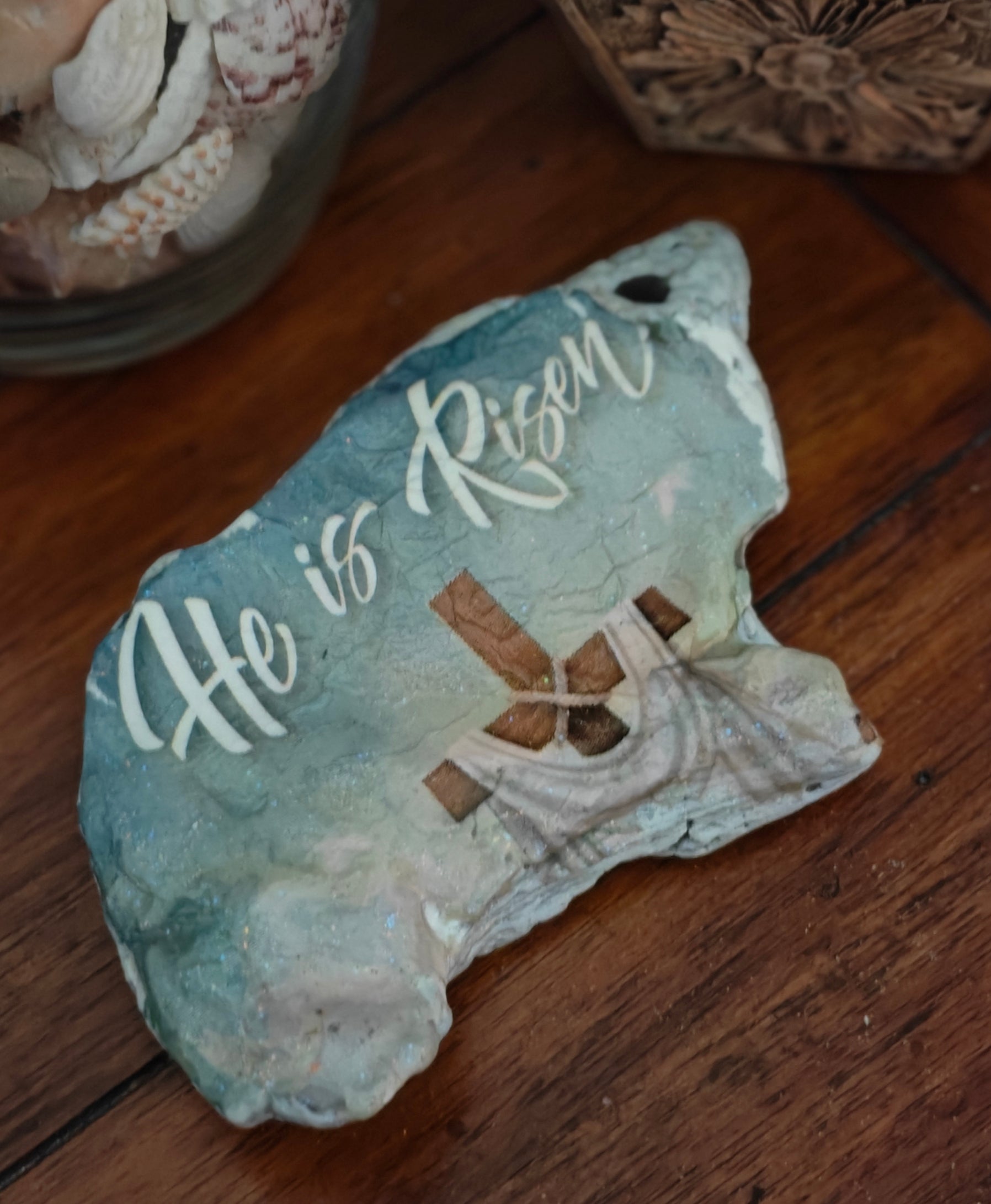 “Hand‑decorated small natural shell featuring the message ‘He Is Risen’