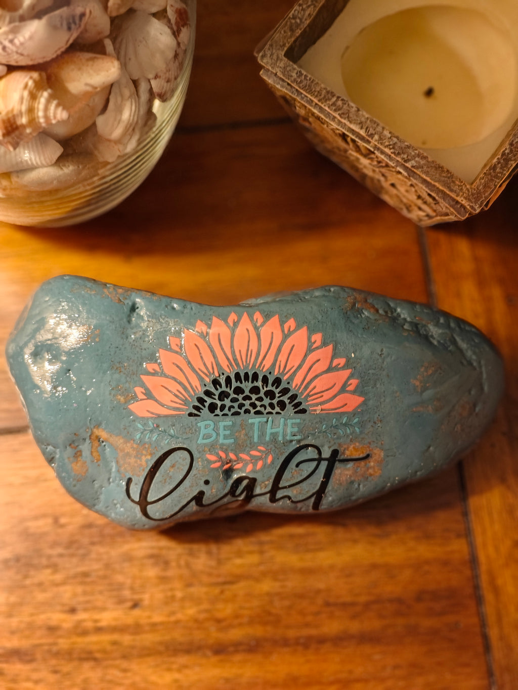 “This hand‑decorated gray‑blue stone features the uplifting message ‘Be the Light’.