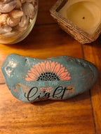 “This hand‑decorated gray‑blue stone features the uplifting message ‘Be the Light’.