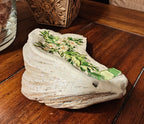 “Hand‑decorated small off‑white shell featuring a green cross accented with cheerful daisies.